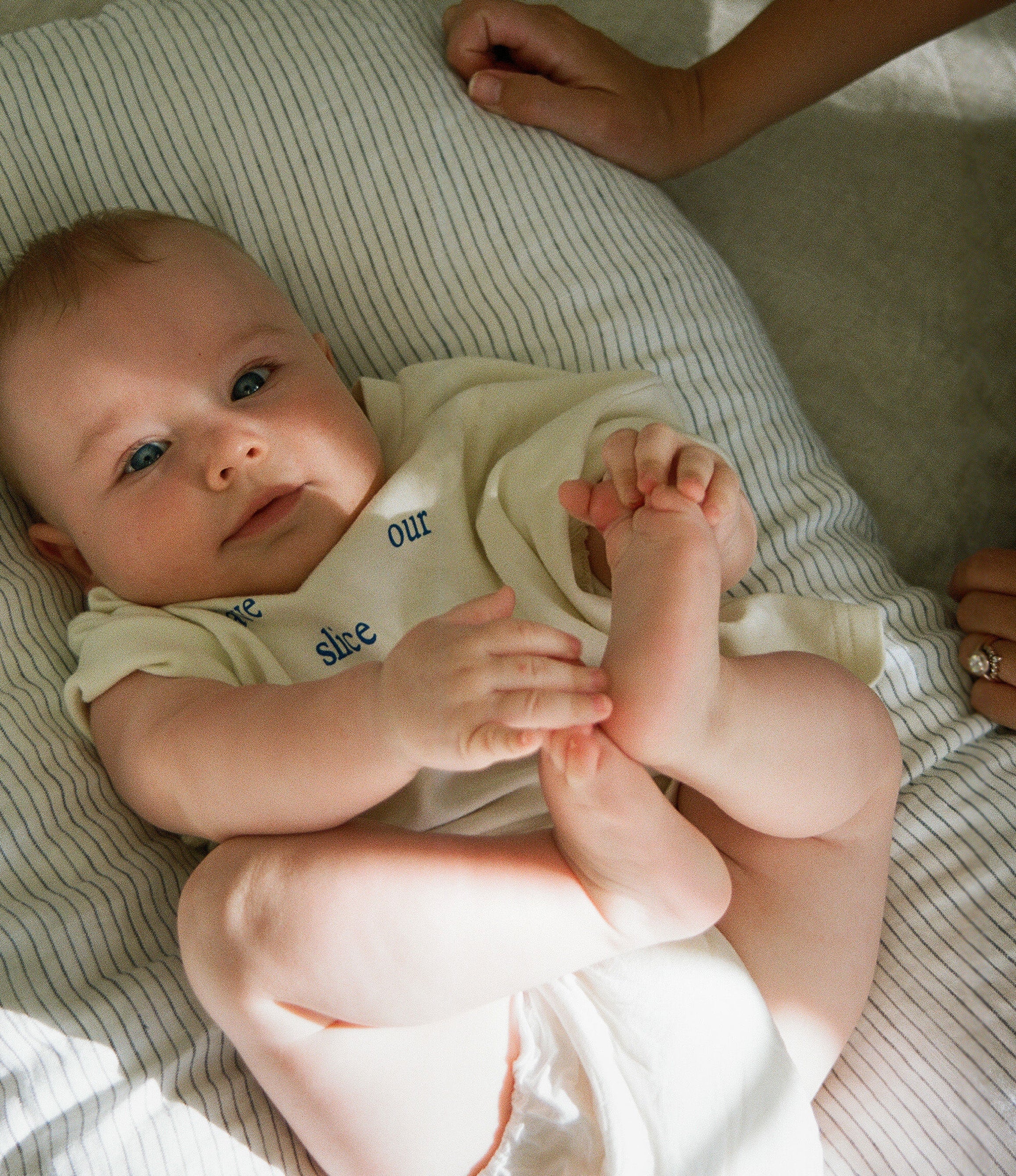 Baby Laying In A Pinstripe Bubba Cloud Baby Lounger. Baby Is Looking At The Camera With Blue Eyes Wearing A White Body Suit.